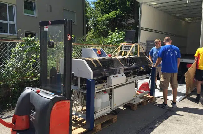Mitarbeiter der Tip Top Umzug GmbH verpacken eine große Maschine in einen LKW