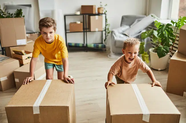 Zwei Kinder verschieben lachend verpackte Umzugkartons